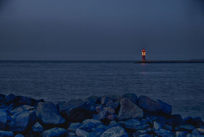 Lighthouse by sea against clear sky during sunset