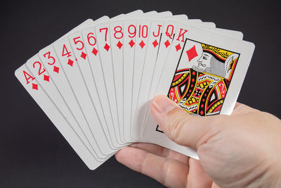 Cropped image of hand holding playing card against black background