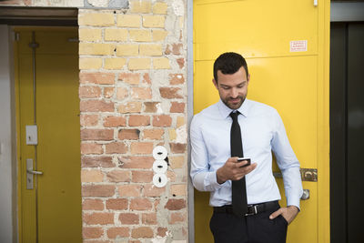Businessman leaning in front of elevator using smartphone