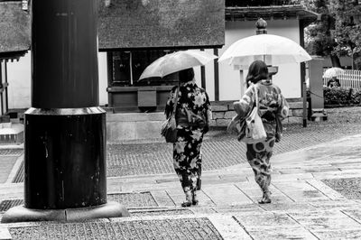Women with umbrellas walking on footpath in city