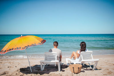 Rear view of people at beach against clear sky