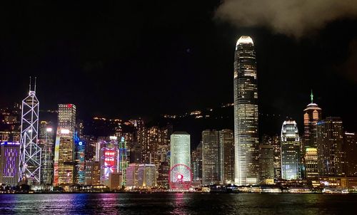 Illuminated buildings by river against sky at night