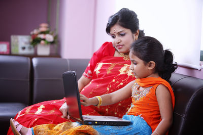Mother and daughter using laptop while sitting on sofa at home