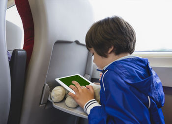 Rear view of boy using digital tablet sitting in airplane