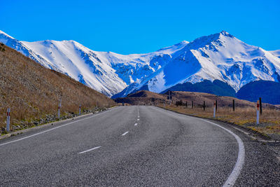 Road by snowcapped mountains against clear blue sky