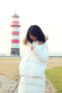 Young woman standing by lighthouse against clear sky