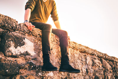 Low section of man sitting on rock against sky
