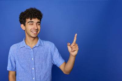 Portrait of young woman gesturing while standing against blue background