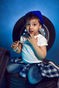 Boy in a white t shirt shirt and hat sits on a background of car wheels on a blue