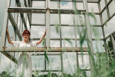 Low angle portrait of young woman standing amidst metallic structure