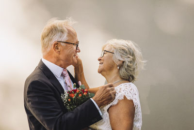 Side view of smiling senior couple looking at each other standing against wall