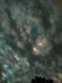 Low angle view of trees against cloudy sky