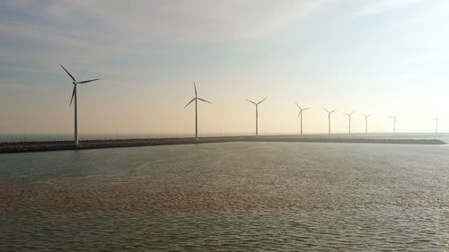 Wind turbines on landscape against sky during sunset
