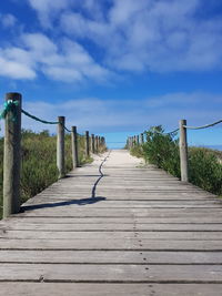 Empty wooden boardwalk amidst plants against sky