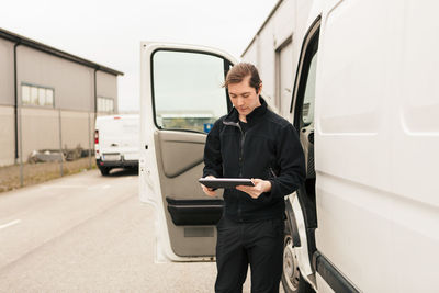 Manual worker using digital tablet by delivery van while standing on road