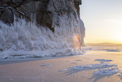 Snow covered mountain at sea against sky during sunset