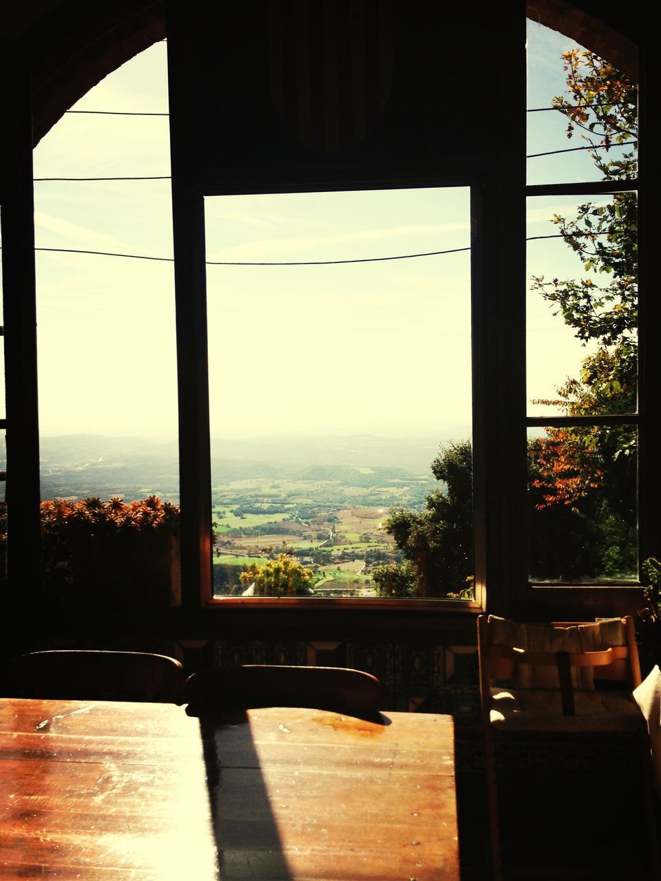 indoors, window, glass - material, transparent, table, chair, built structure, looking through window, architecture, restaurant, sea, home interior, silhouette, sky, absence, glass, tree, clear sky, sunlight, sunset