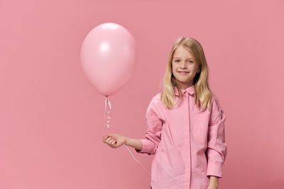 Young woman holding balloons against pink background