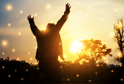 Rear view of silhouette woman with arms raised against sky during sunset