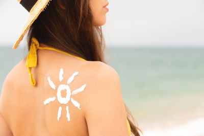 Happy girl with the sun on her back by the sea in nature. drawing with cream in the shape of a sun