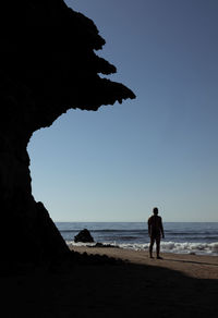 Rear view of man in swimwear standing on beach against cliff