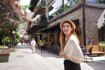 Portrait of young woman standing against buildings