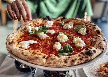 Midsection of man with hand reaching out for bufalina pizza on table.