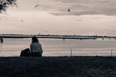 Man sitting by river against sky