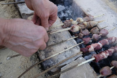 High angle view of man cooking meat skewers on barbecue