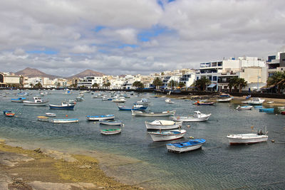 Boats moored at harbor in city against sky