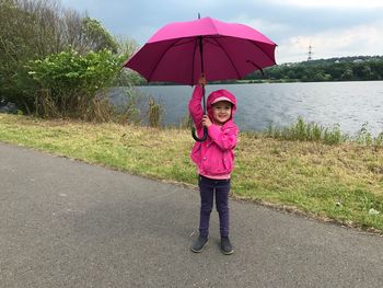 Full length portrait of girl standing by pink umbrella against sky