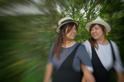Sisters in hats looking at each other against trees