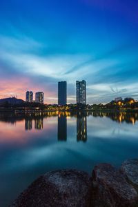 Illuminated city by lake against sky at night