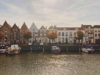 Buildings by river against sky in city