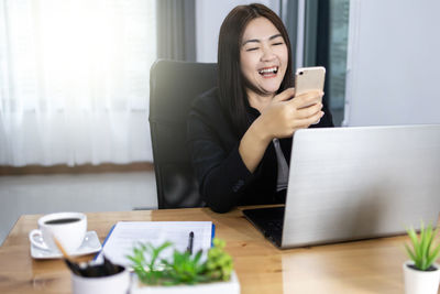 Mid adult woman using mobile phone while sitting on table