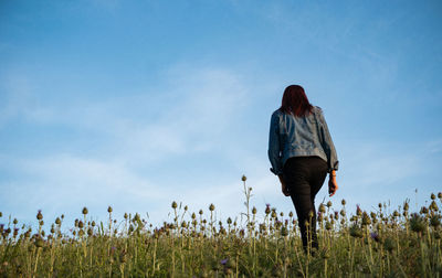 Rear view of woman walking on field against sky