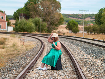 Side view of woman with suitcase sitting on railroad track