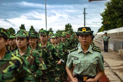 Female army soldiers standing on road against cloudy sky