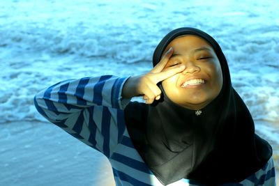 Portrait of cheerful teenage girl gesturing peace sign at beach