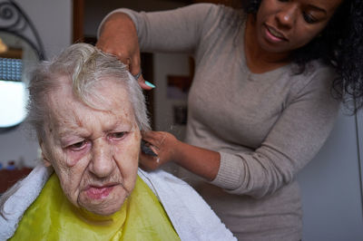 Caring african american woman caregiver, cutting her elderly woman hair at home