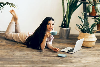 Portrait of woman holding coffee cup lying on floor