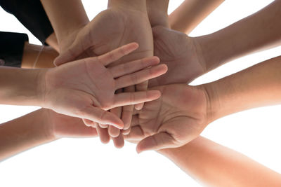 Low angle view of people joining hands over white background