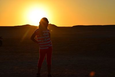 Rear view of woman standing on field during sunset