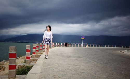 Woman walking along beach against cloudy sky