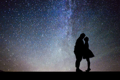 Side view of silhouette couple romancing while standing against star field at night