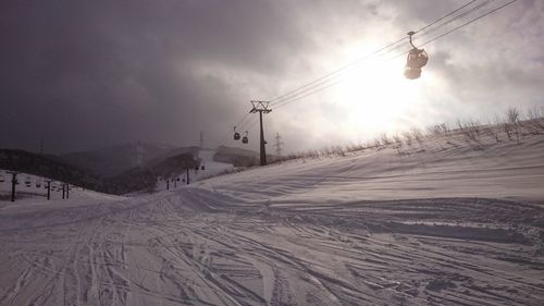 Overhead cable car at snow covered field against sky during sunset