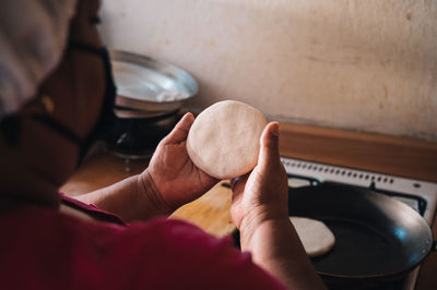 Back view of crop unrecognizable ethnic female preparing venezuelan arepas in pan on gas stove in kitchen