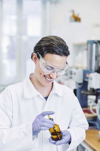 Happy female scientist using pipette while examining chemical in laboratory