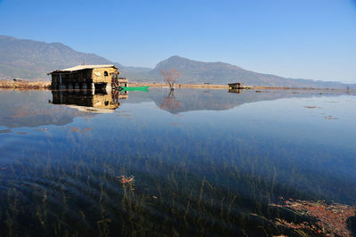 Cottage reflecting in lake against sky