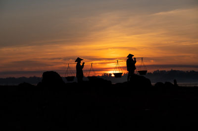 Silhouette people standing on shore against sky during sunset